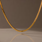 The Twisted Snake Chain Necklace is shown on a neutral background with a soft reflection below, making it an ideal choice for modern, layered jewelry styles.