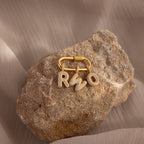 A gold keyring with Pave Bubble Letter Charms, each charm elegantly studded with diamonds in the letters R, S, and O, rests on a textured rock.