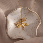 The Pave Bubble Letter Charm gold necklace with heart and wing rests on a speckled ceramic dish, set against a beige fabric background.