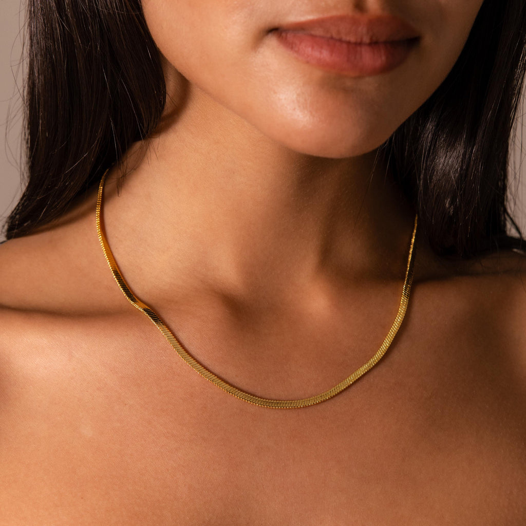 A woman wears the Twisted Snake Chain Necklace against her bare neck and shoulders, showcasing a modern and minimal necklace style.