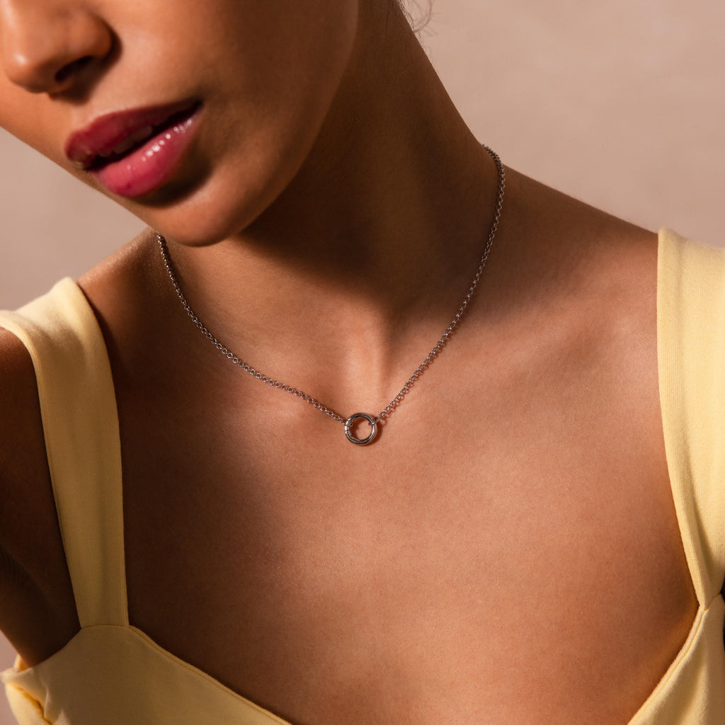 A woman in a yellow top wears the Cable Circle Charm Necklace in Silver, featuring a circular charm—a perfect statement piece to elevate any layered necklace style.