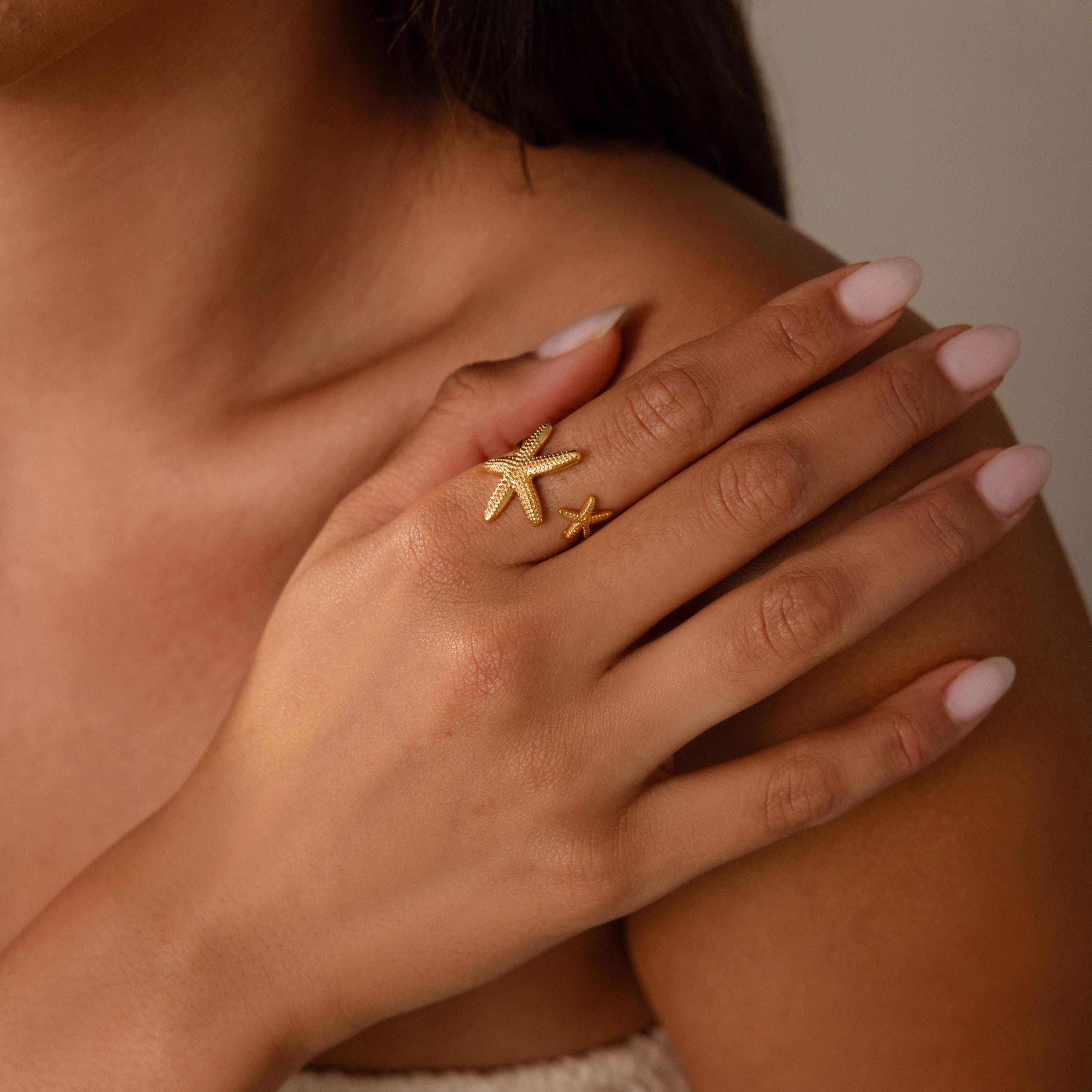 Woman with light pink nails wears the Open Duo Starfish Ring, a gold coastal-inspired statement piece, on her finger as her hand rests on her shoulder.