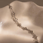The Clover Station Bracelet in Silver, featuring clover-shaped links, is displayed on a cream-colored textured shell-shaped dish.