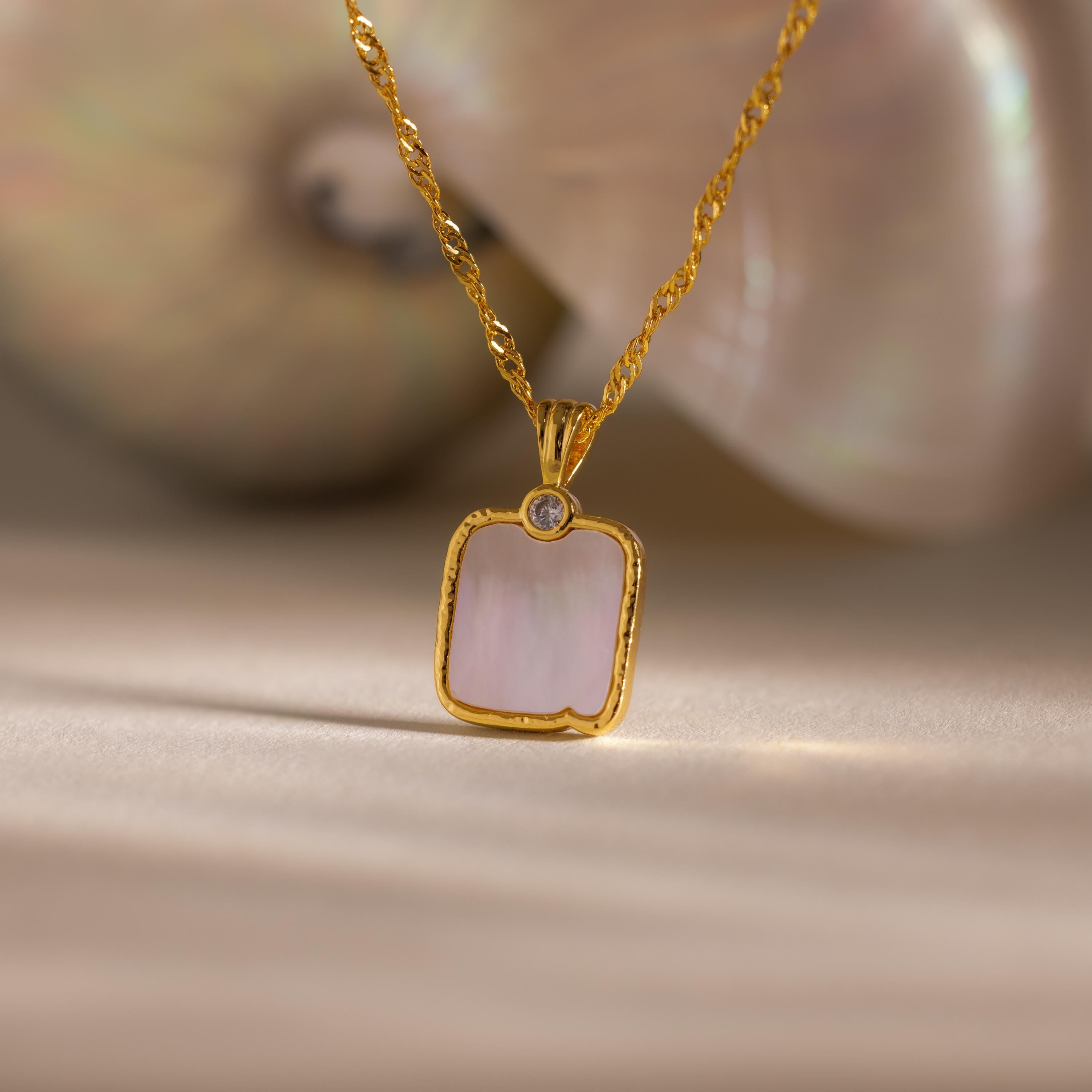 The Square Mother of Pearl Necklace features an iridescent pendant with a small gem, displayed beautifully on a neutral background.
