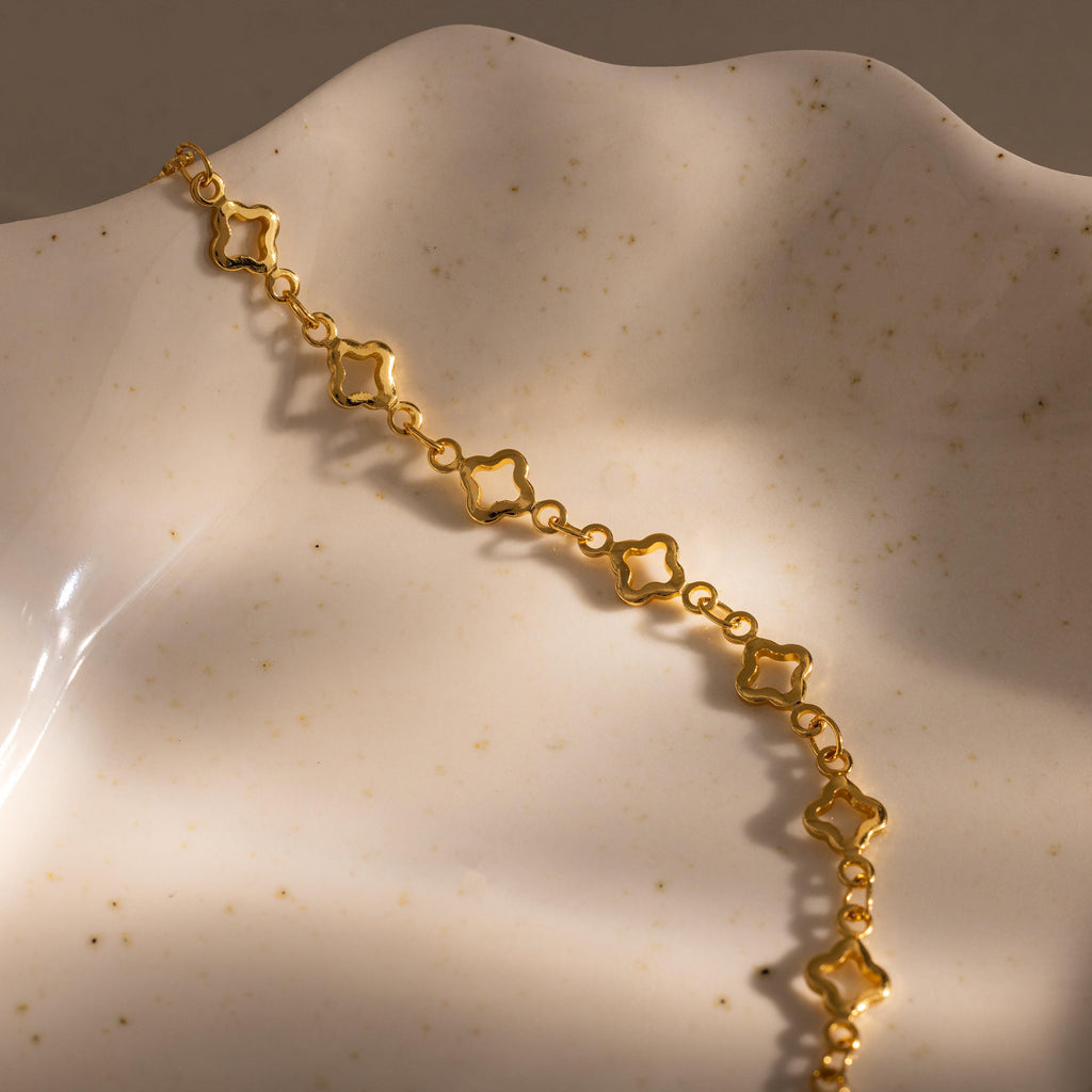 The Clover Station Bracelet in 18K Gold, featuring floral-inspired clover links, is showcased on a wavy, speckled ceramic surface.