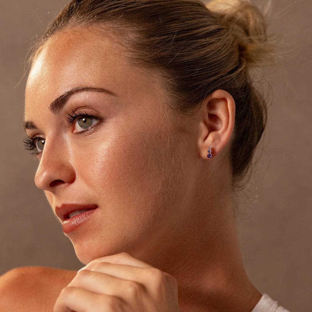 Woman with blonde hair in a bun wears Ombre Birthstone Flatback Studs, gazing thoughtfully to the side—a perfect personalized gift for any occasion.