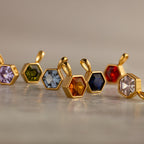 Hexagon Birthstone Charms with faceted, colorful gemstones are lined up on marble—a striking showcase of geometric jewelry.
