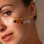 Woman holding a gold necklace with five colorful Hexagon Topaz Charms across her face, showcasing vibrant geometric jewelry.