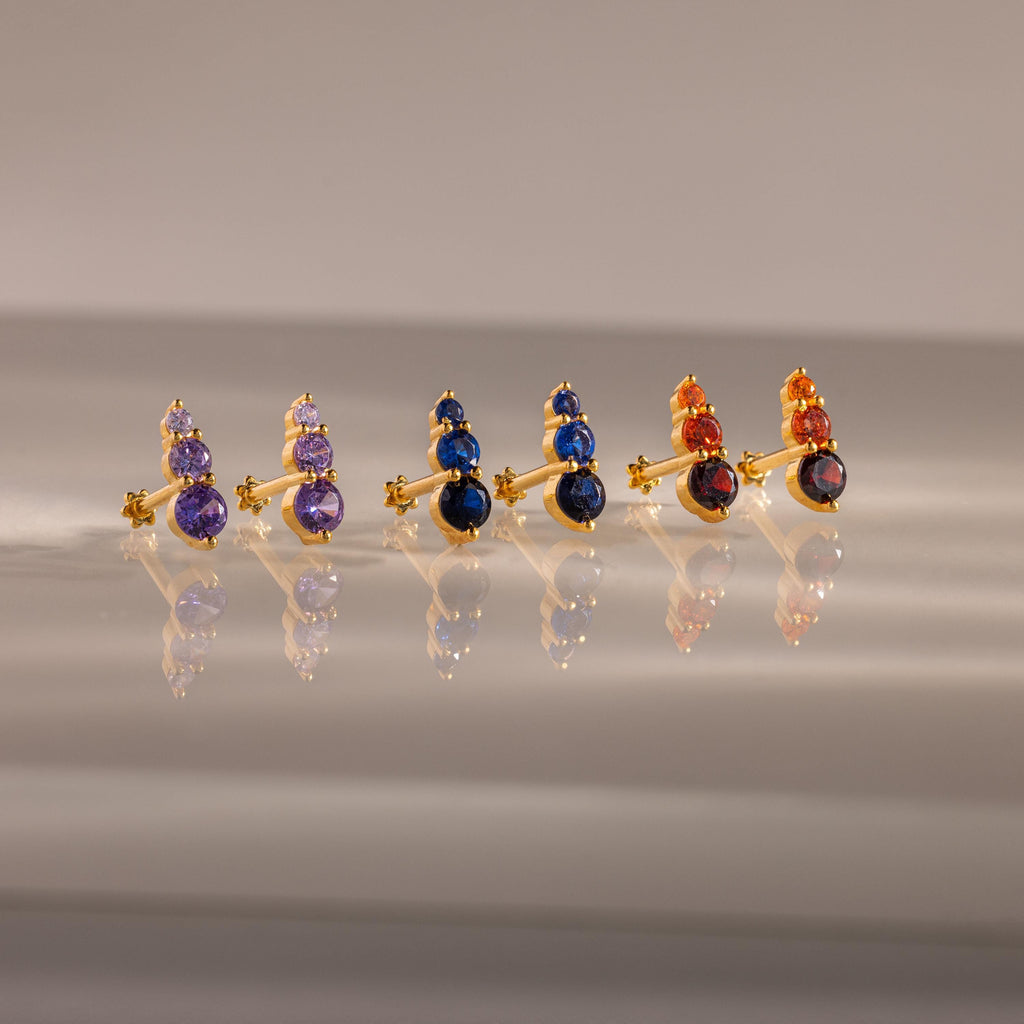 The Ombre Birthstone Flatback Studs feature three gold pairs with purple, blue, and orange gemstones—perfect for a personalized gift.
