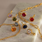 Elegant gold geometric jewelry featuring the Hexagon Topaz Charm with faceted stones in various colors, beautifully displayed on a marble surface.