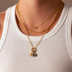 Close-up of layered gold necklaces with geometric pendants, featuring the Hexagon Birthstone Charm, worn over a white ribbed tank top.