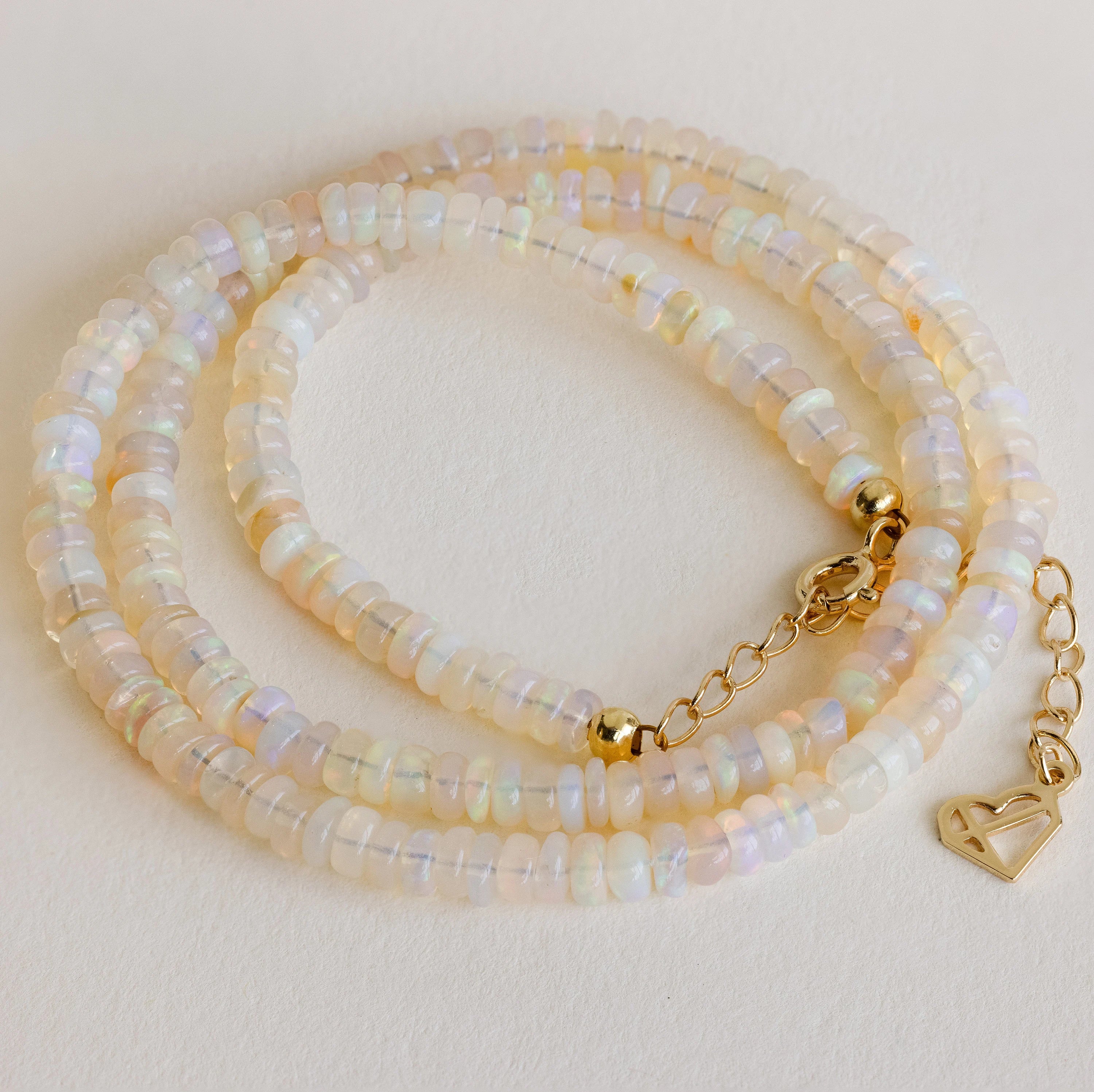 The Opal Beaded Necklace features iridescent beads, a gold clasp, and a heart-shaped charm—adding bohemian flair and shimmering beauty to any look.
