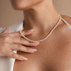 A woman with manicured nails touches the Opal Beaded Necklace on her neck, wearing a white top and highlighting this elegant bohemian jewelry piece.