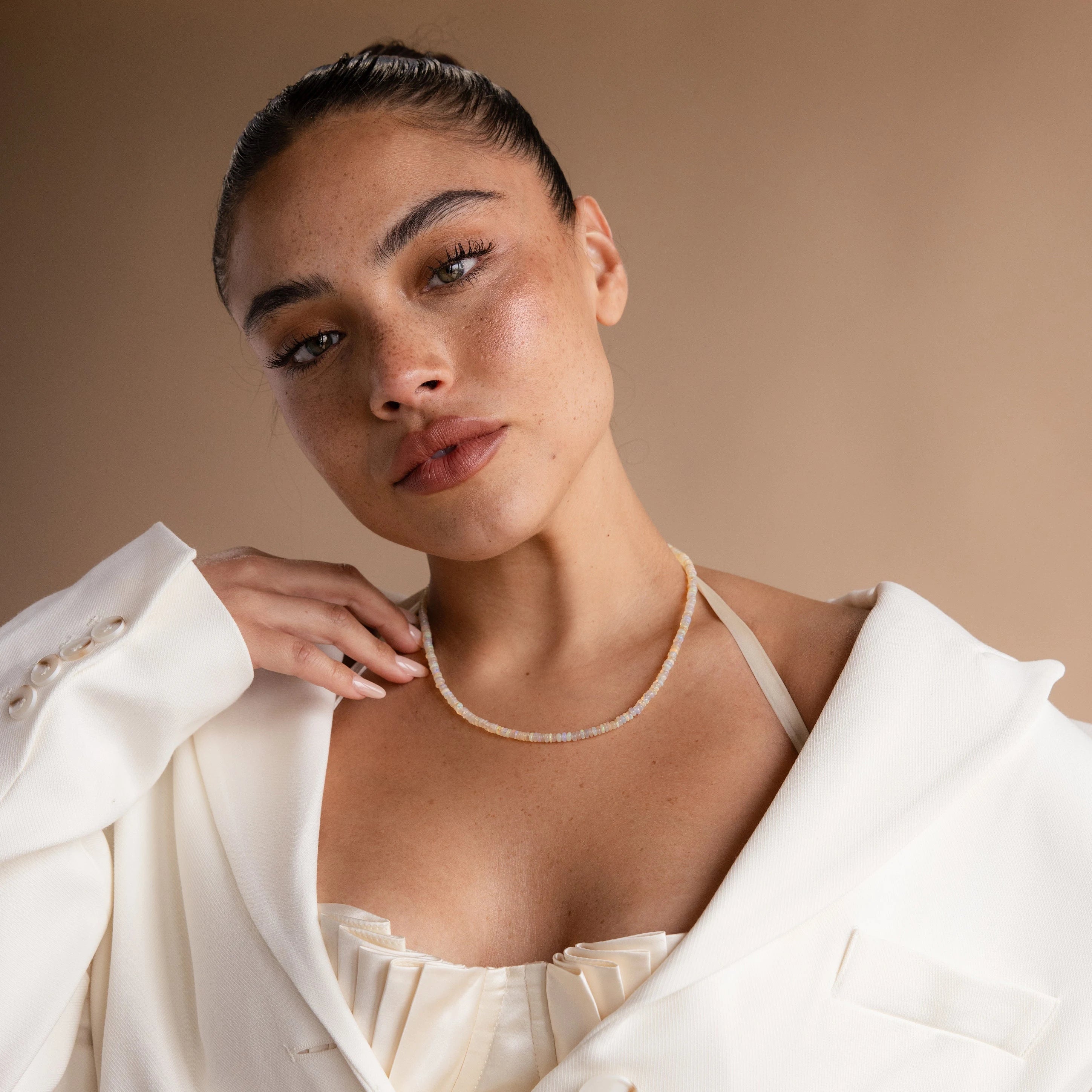 A woman in a white outfit wears the Opal Beaded Necklace, posing against a beige background—a gorgeous bohemian jewelry accent.