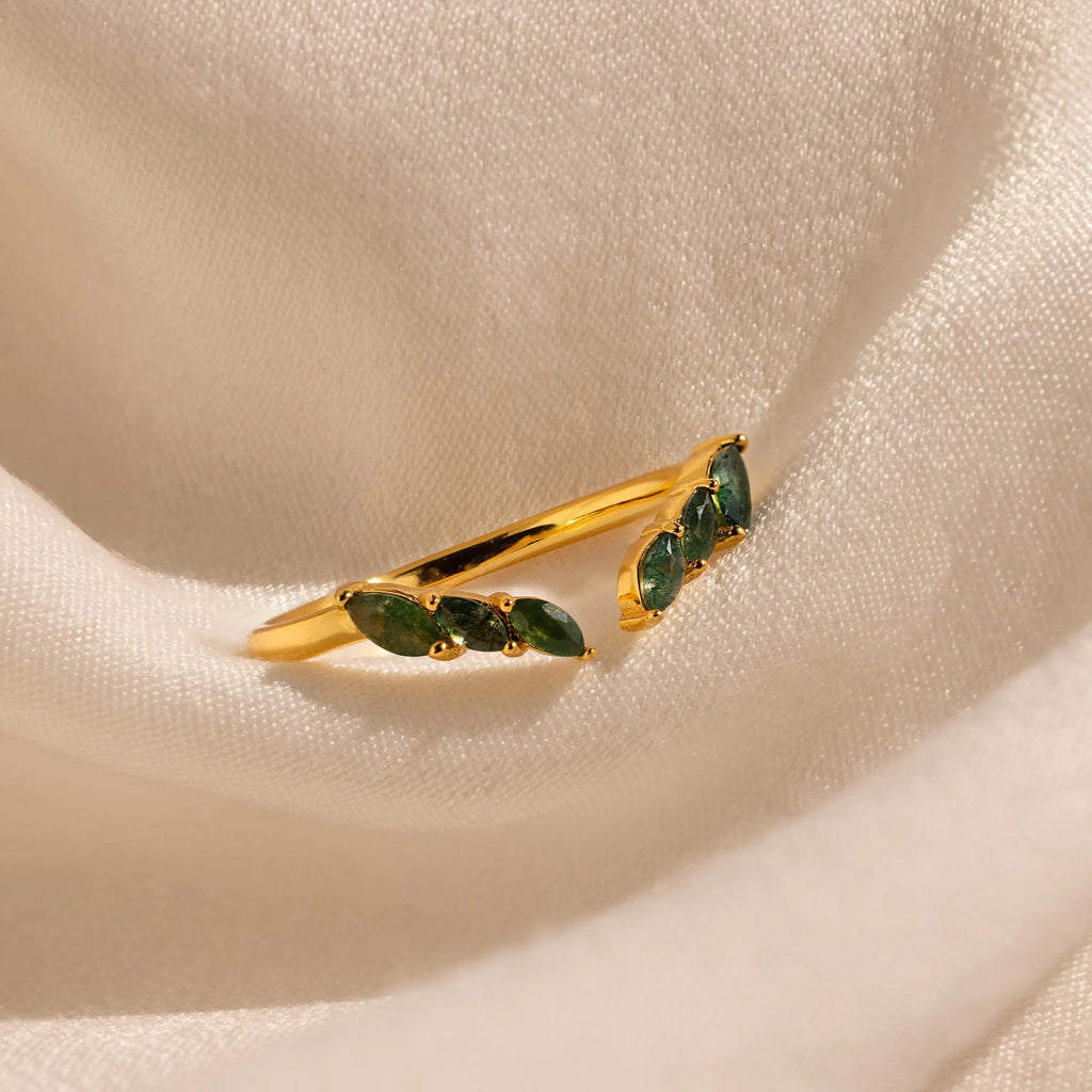 The Open Moss Agate Chevron Ring features three green stones set in gold and displayed on cream draped fabric—a dainty, unique promise ring option.