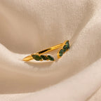 The Open Moss Agate Chevron Ring features three green stones set in gold and displayed on cream draped fabric—a dainty, unique promise ring option.
