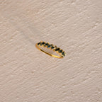 The Moss Agate Eternity Ring, featuring a nature-inspired zigzag pattern, rests on a textured beige surface, embodying organic elegance.