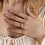 A woman's hand with nude nails rests on her chest, adorned with the Moss Agate Eternity Ring featuring gold and green baguette-cut gemstones.