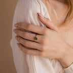 A woman with nude nails wears the Agate Teardrop Ring, its polished green stone sparkling as she gently rests her hand on her shoulder.