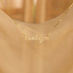 The Pave Dream Script Name Necklace, featuring "Evelyn" in cursive pavé letters, shimmers beautifully against a soft beige background.