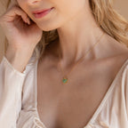 A woman wearing a light blouse gently touches her face while showcasing the Aventurine Heart Necklace, featuring a gold chain and a green heart-shaped pendant.
