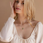 A blonde woman in a white blouse wears the Aventurine Heart Necklace, featuring a green heart-shaped pendant.