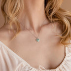 A woman wears an off-the-shoulder white top with the Aventurine Heart Necklace, featuring a green, heart-shaped aventurine gemstone pendant.