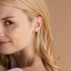 Close-up of a smiling blonde woman wearing Emerald Teardrop Huggies.