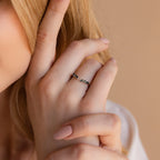 A blonde-haired woman touches her face, highlighting the Open Moss Agate Chevron Ring—a delicate promise ring with green stones—on her finger.