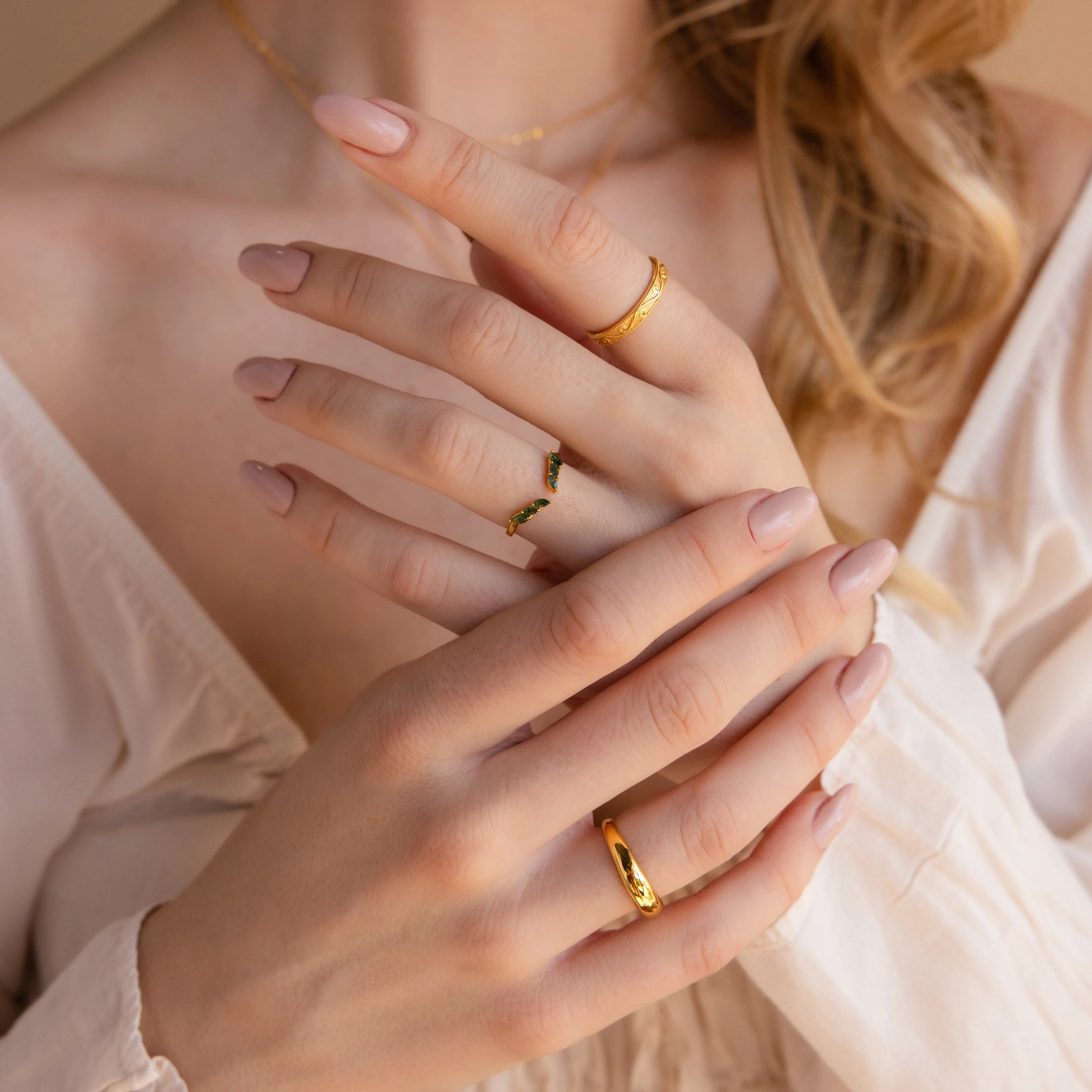 Woman with manicured nails wearing the Open Moss Agate Chevron Ring and gold bands, hands gently crossed, styled with a cream-colored blouse.