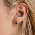 Close-up of a woman's ear wearing Emerald Teardrop Huggies—dainty hoop earrings with a small gold setting and a green gemstone.