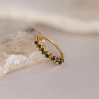 The Moss Agate Eternity Ring is a gold band featuring a row of baguette-cut green stones, elegantly displayed on a lightly textured stone surface.