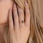 A hand with nude nails wears the Agate Teardrop Ring, showcasing a green moss agate gemstone and sparkling accent stones set in gold.