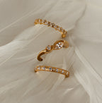 The Diamond Eternity Ring shines among three gold rings, set on soft white fabric with a feather-like texture.