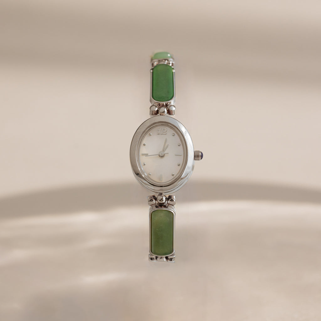 A vintage-style Jade Band Timepiece watch with a silver-tone oval case, white dial, and green rectangular stone links on a matching bracelet, shown against a warm beige background.