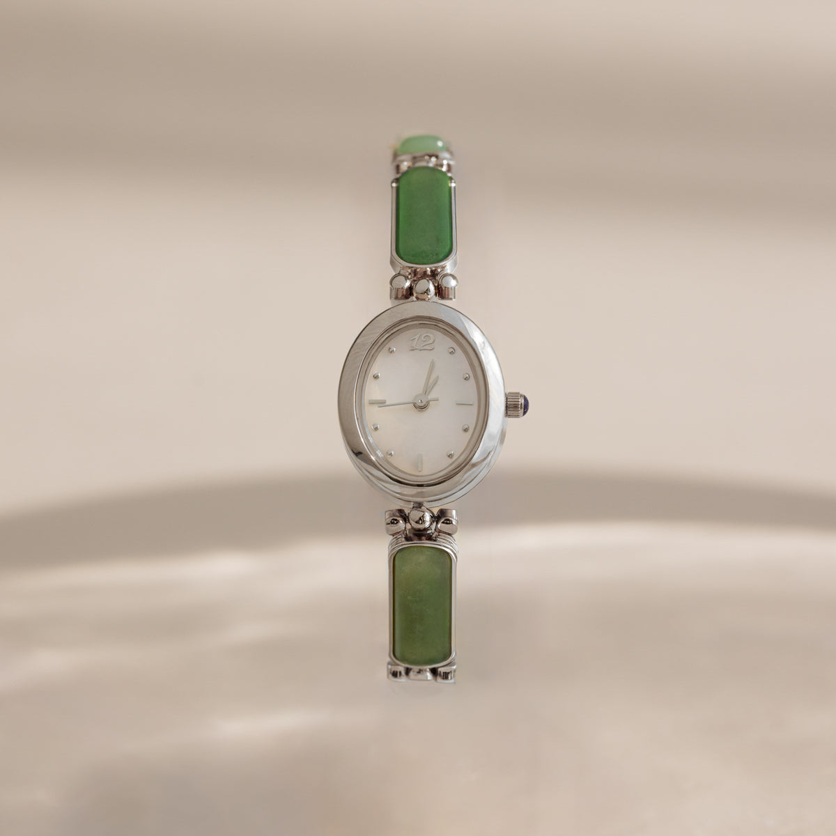 A vintage-style Jade Band Timepiece watch with a silver-tone oval case, white dial, and green rectangular stone links on a matching bracelet, shown against a warm beige background.