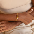 A close-up of a person's wrist wearing a delicate gold chain rolo bracelet with a small charm featuring the letter 'E'