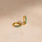 Gold hoop earrings with green opal stones on a beige background