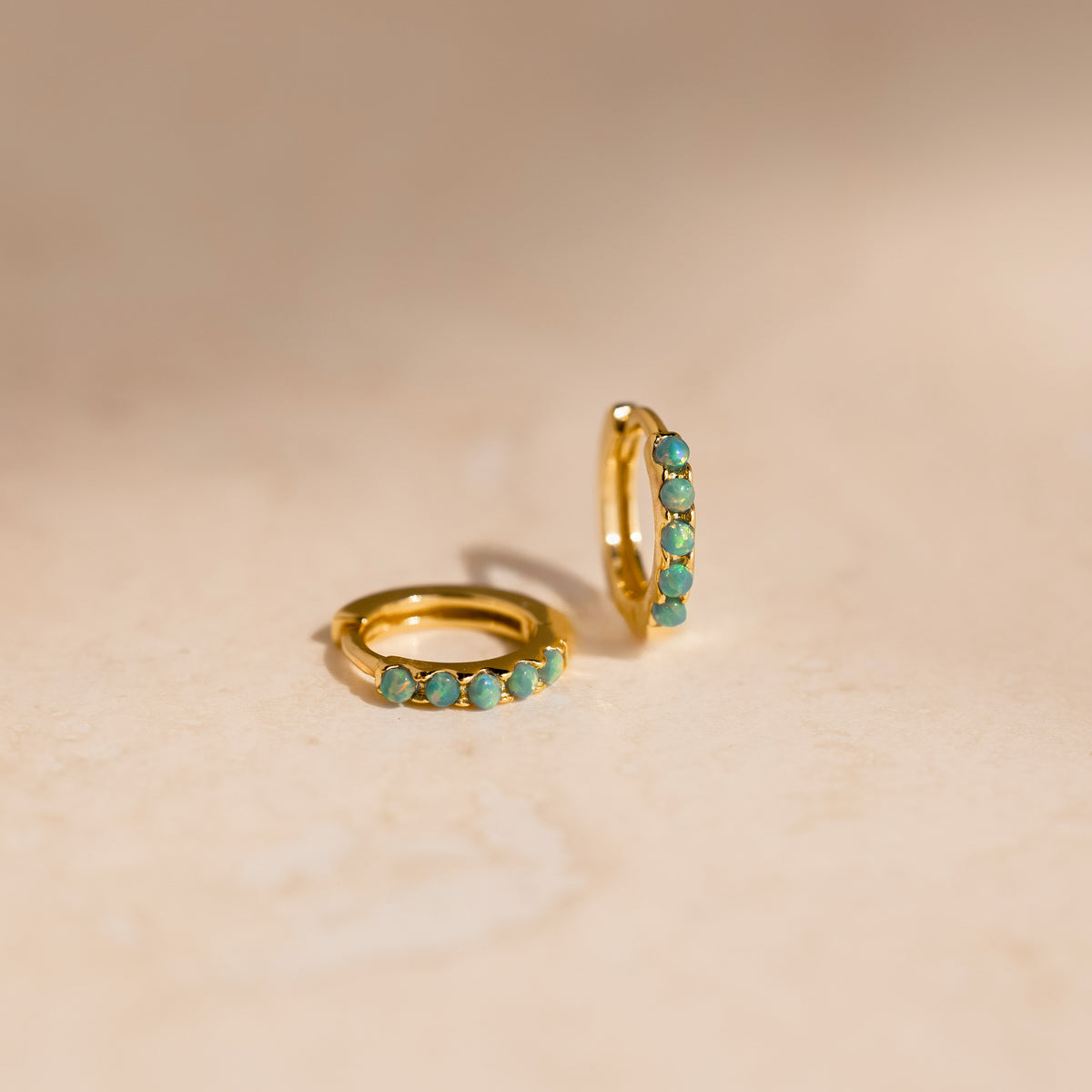 Gold hoop earrings with green opal stones on a beige background