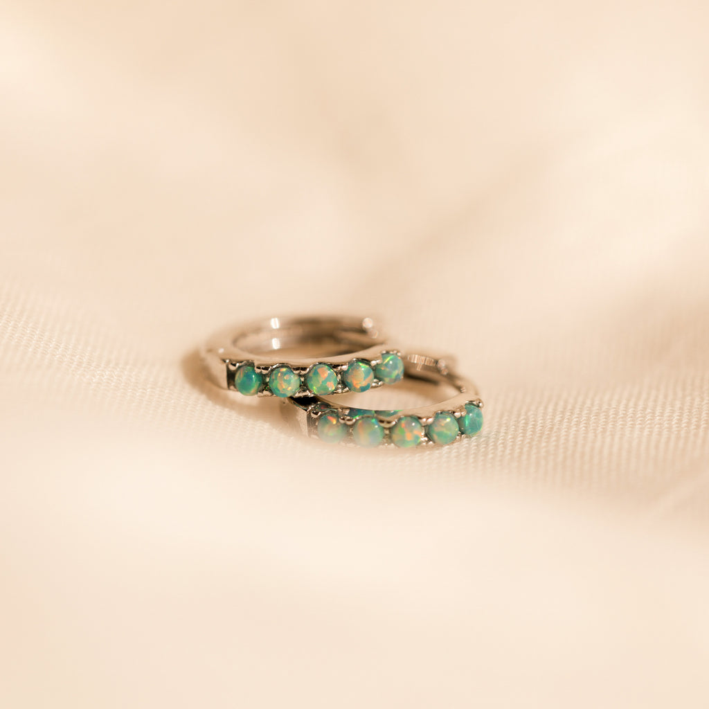 Close up of our Garden Green Opal Huggies in silver on a beige fabric background