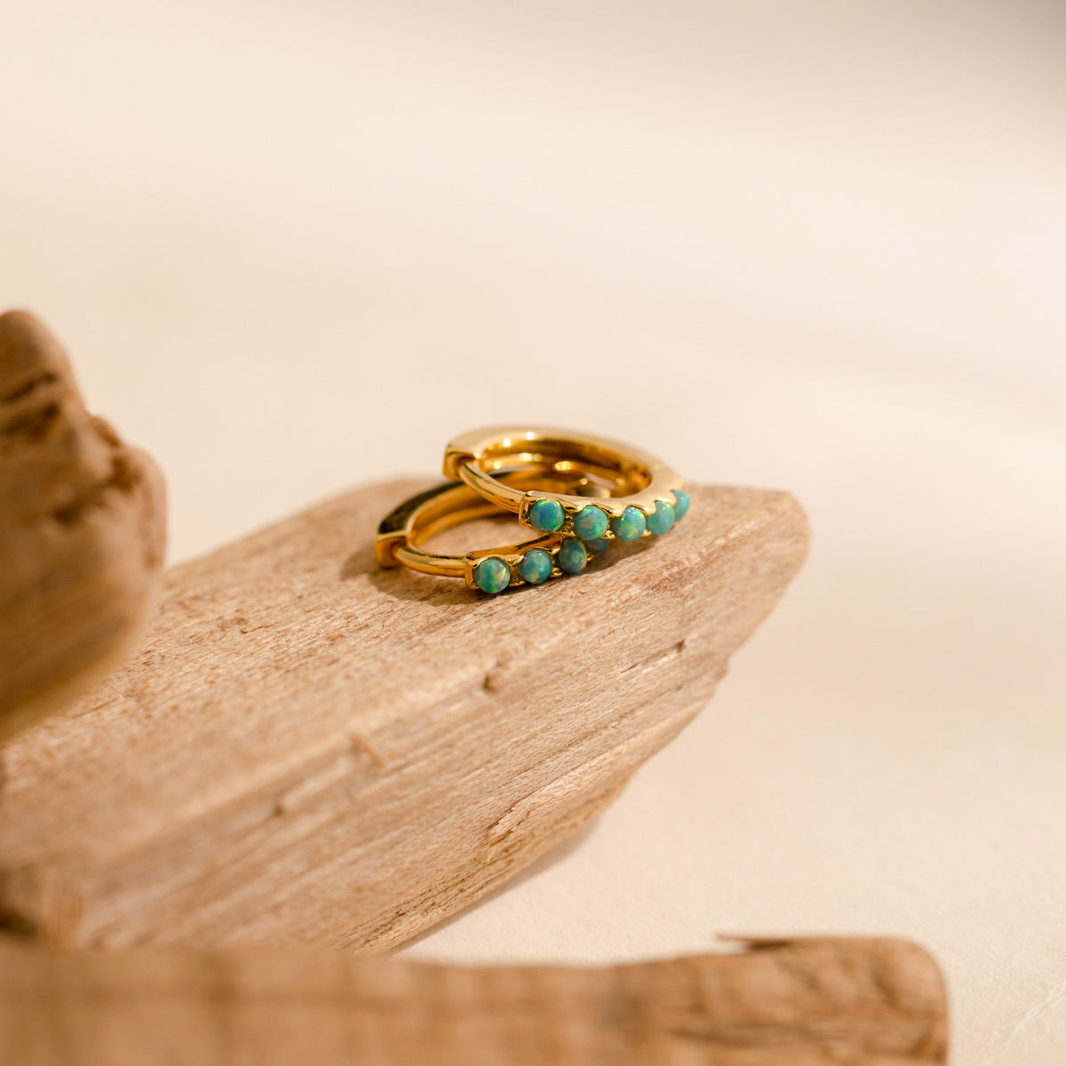A pair of our Garden Green Opal Huggies displayed on a piece of natural driftwood against a soft beige background.
