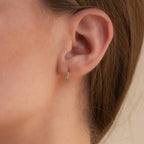 Close-up of an ear wearing our Garden Green Opal Huggies earring with a blurred background