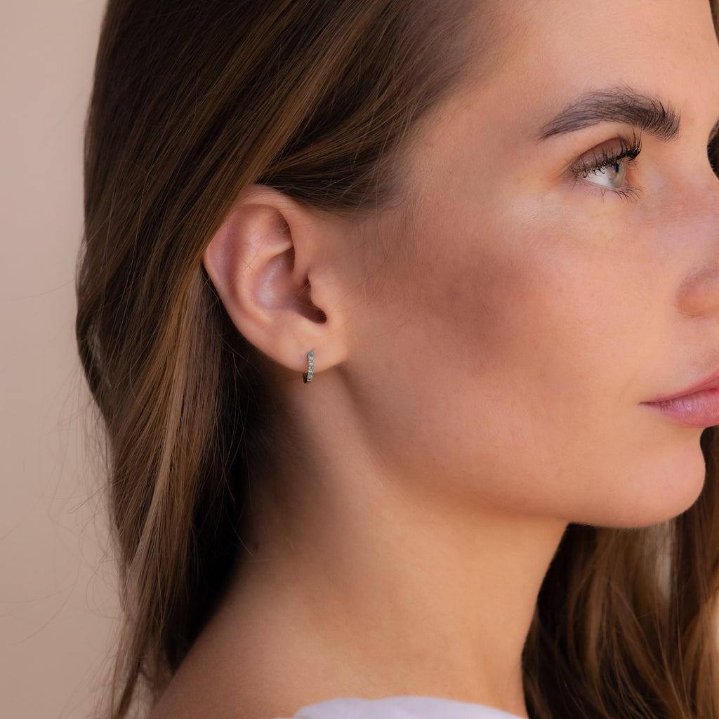 Close-up of a woman wearing our Garden Green Opal Huggies in silver with a neutral background