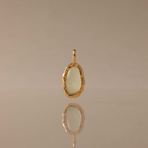 Aura Seafoam Charm: oval seafoam stone in organic textured gold setting, reflected on a shiny surface.