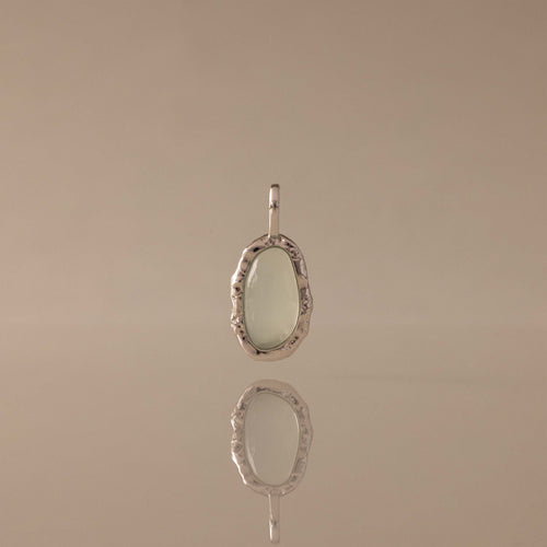 Aura Seafoam Charm: oval seafoam stone in an organic silver-toned setting, reflected on a surface.