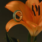The Haven Jade Spinner Ring rests delicately on the petal of an orange lily, its gold band shimmering against a dark background.