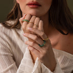 A woman in a cream sweater displays her hands, one adorned with the gleaming Haven Jade Spinner Ring, gold band, and green bangles as her lips rest softly parted.