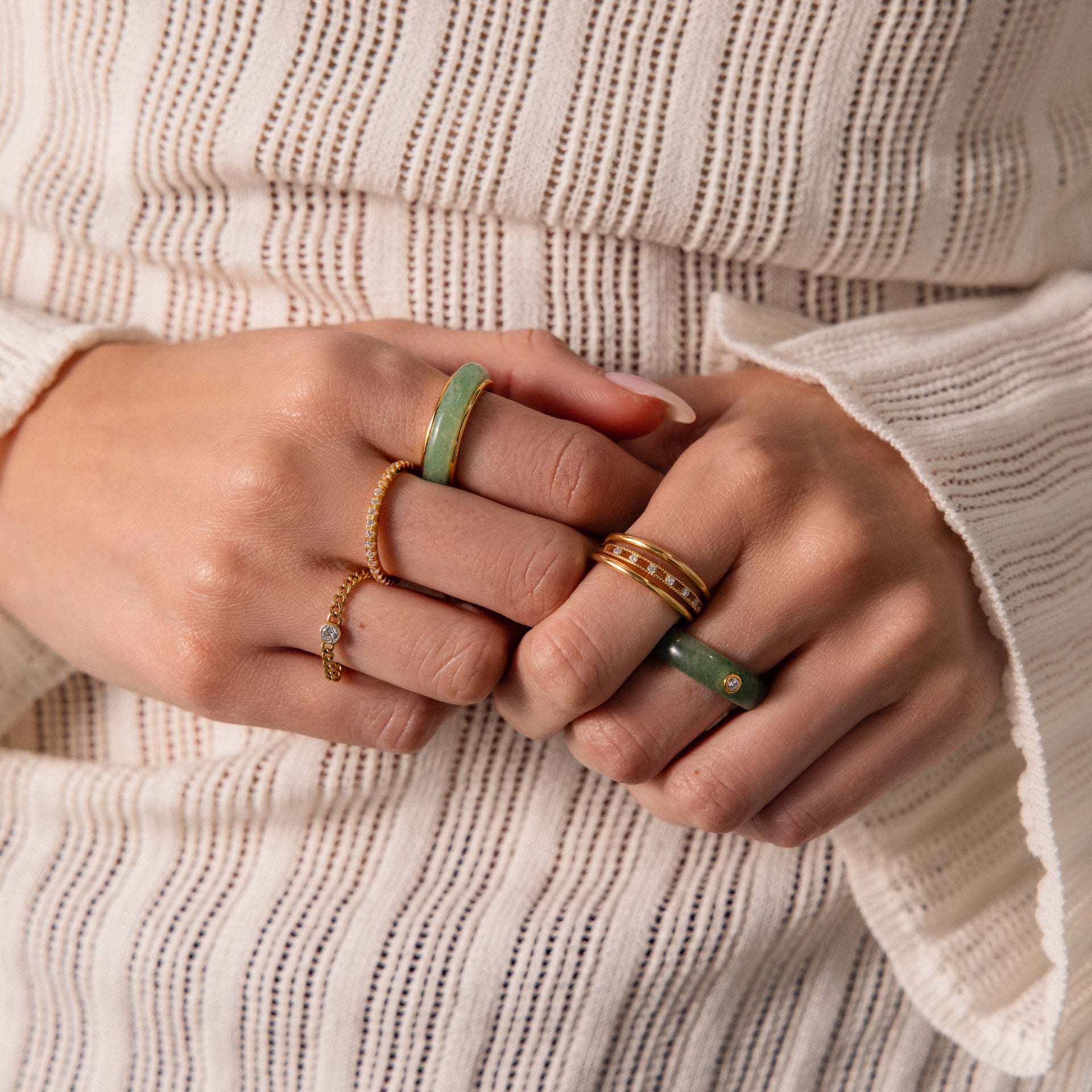 Close-up of hands wearing a gold band and the Haven Jade Spinner Ring, paired with a white textured long-sleeve top—an elegant display of mindful jewelry.