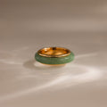 The Haven Jade Spinner Ring features a thick green jade band set in gold, resting elegantly on a smooth, light-colored surface.