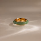 The Haven Jade Spinner Ring features a thick green jade band set in gold, resting elegantly on a smooth, light-colored surface.